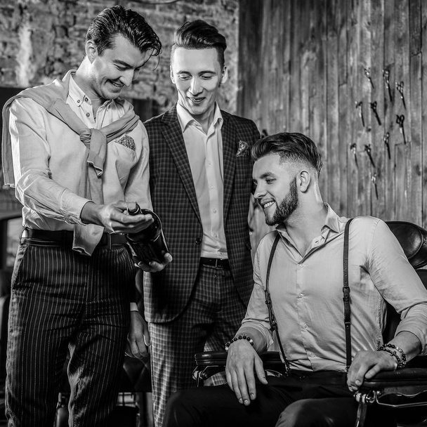 Three young elegant positive friends pose in interior of barbershop. Black-white photo. - Foto, Imagem