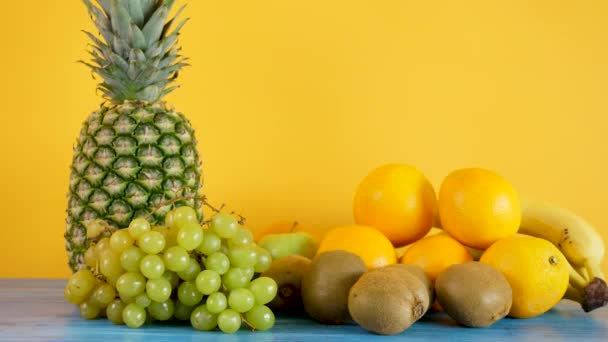 Orangen, Bananen, Ananas, Kiwi und Trauben auf gelbem Hintergrund - Filmmaterial, Video