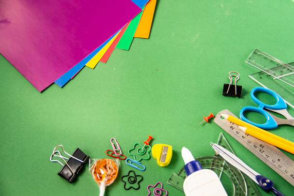 Plumas de fieltro, lápices, clips, crayones, reglas, pegamento, marcador corrector y papel de color sobre un fondo verde
 - Foto, imagen
