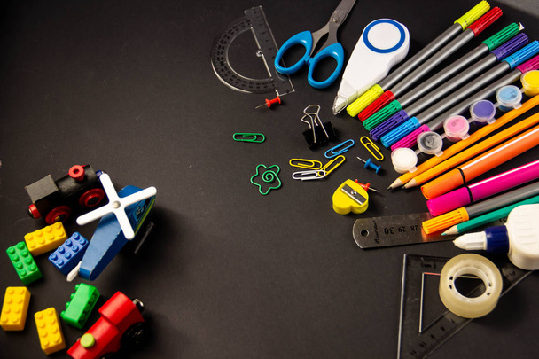 Felt pens, pencils, paperclips, crayons, rulers, glue, proofreader, marker, scissors, notebook sharpener on a black background with space under the text - Photo, Image