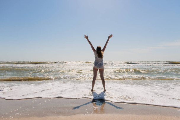 Silhouette of young woman with hands up at beach. - Photo, Image
