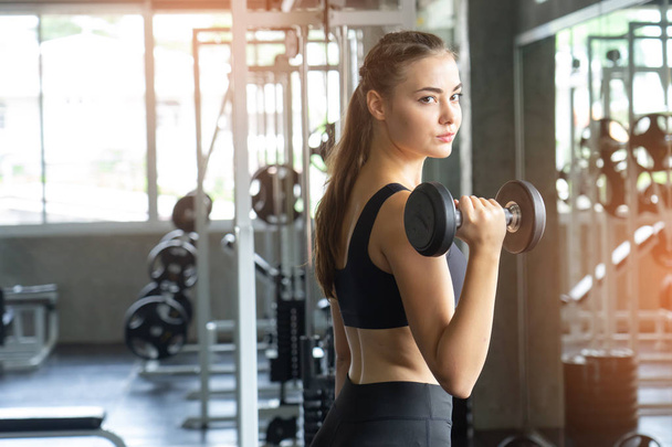 Muscular young woman with beautiful  body doing exercises with dumbbell. Sporty girl lifting weights in gym. - Photo, Image