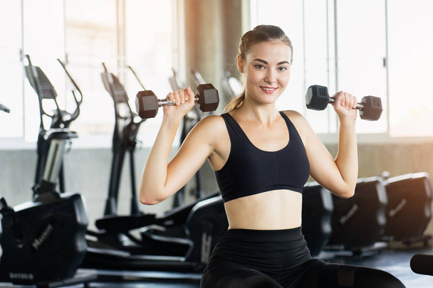 Muscular young woman with beautiful  body doing exercises with dumbbell. Sporty girl lifting weights in gym. - Foto, Imagem