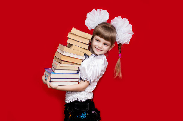 Маленькая девочка держит много книг, изолированных на красный. Понятие знаний или школы. Любитель книг
 - Фото, изображение