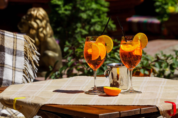 Aperol spritz cocktail in glas op houten tafel tegen een heldere zonnige café. Twee glazen met een cocktail en een ijsemmer op tafel. - Foto, afbeelding