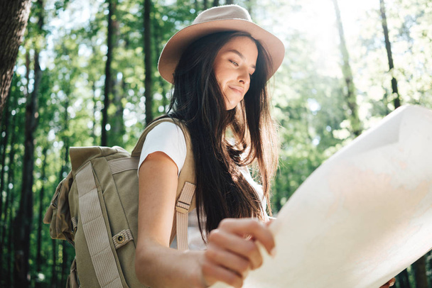Smiling breave girl with travel backpack, and location map in hands looking directional way for traveling on outdoors - Foto, Imagem