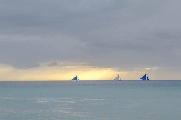 Uitzicht op de zonsondergang in de zee, het strand van Boracay. 2 zeilboten zijn in de zee, de zon achter de wolken. - Foto, afbeelding