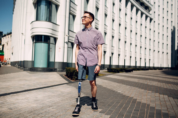 Niepełnosprawny mężczyzna młody z proteza stopy spacery wzdłuż ulicy. - Zdjęcie, obraz
