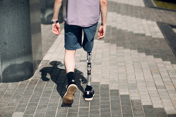 Disabled young man with foot prosthesis walks along the street. - Foto, Imagen