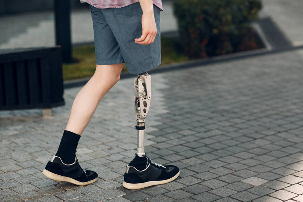 Disabled young man with foot prosthesis walks along the street. - Photo, Image