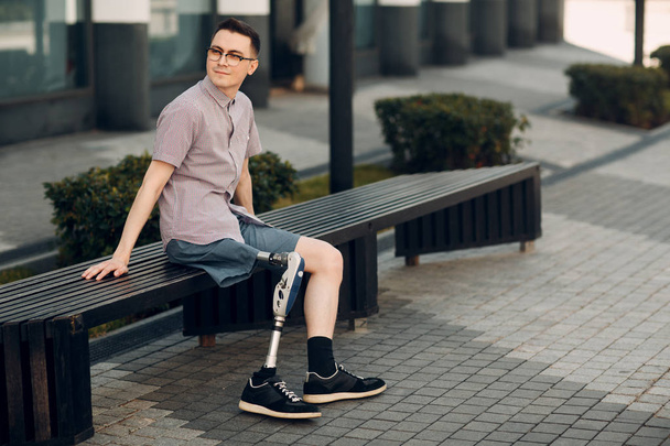 Behinderter junger Mann mit Fußprothese sitzt draußen - Foto, Bild