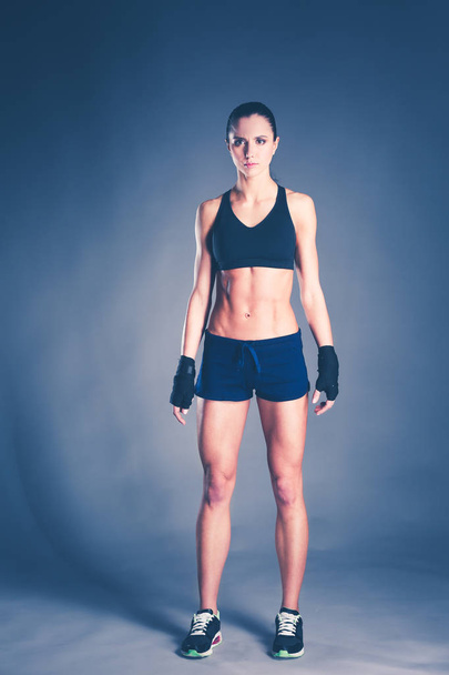 Muscular young woman posing in sportswear against black background. - Foto, Imagen