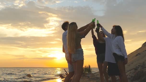 Vrienden rammelende bierflessen op het strand tijdens de zonsondergang. Slow motion. - Video
