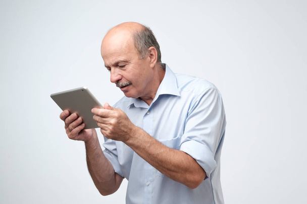 Mature european man using a digital tablet. He is puzzled and confused. He did not know how to use his new gadget - Photo, image