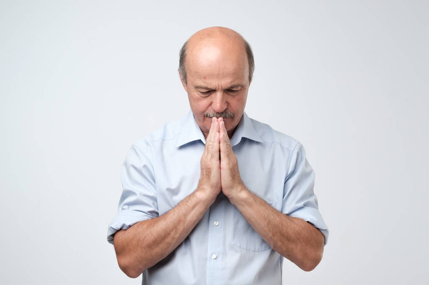 Bild eines reifen Mannes, der die Hände im Gebet oder in der Meditation zusammenlegt, entspannt und ruhig wirkt, träumt und auf das Beste wartet - Foto, Bild
