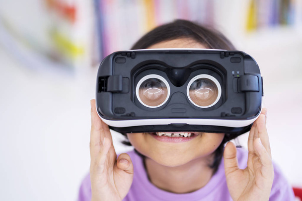 Close up of little girl looks happy while wearing virtual reality glasses in wrong way. Shot at home - Foto, Bild