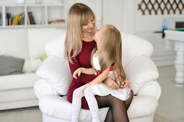 Beautiful mother and daughter are sitting on a white armchair. - Photo, Image