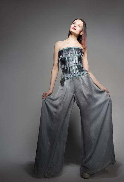 Fashion portrait in full growth, beautiful young woman in wide pants. Stylish in appearance. A neutral grey background - Photo, Image