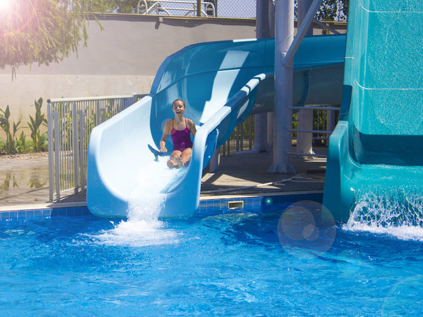 Happy teenage girl going down by the water slide into the pool - Photo, Image