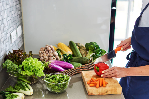 Young woman cooking in the kitchen healthy food, vegetable salad. Holding a knife and cutting vegetables on a cutting board. Healthy lifestyle cooking at home. - Fotó, kép
