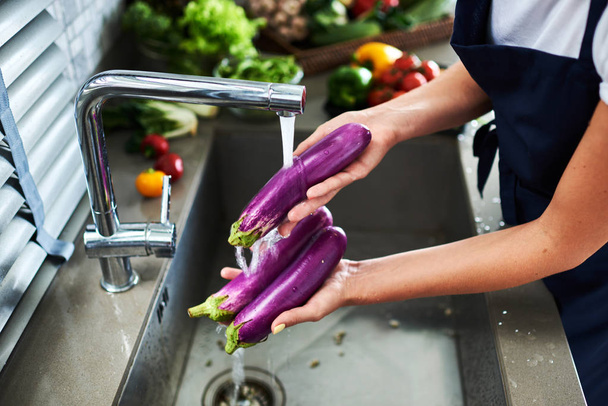 Femme dans un tablier bleu lave les légumes dans l'évier de la cuisine. Image horizontale. Gros plan sur les mains
. - Photo, image