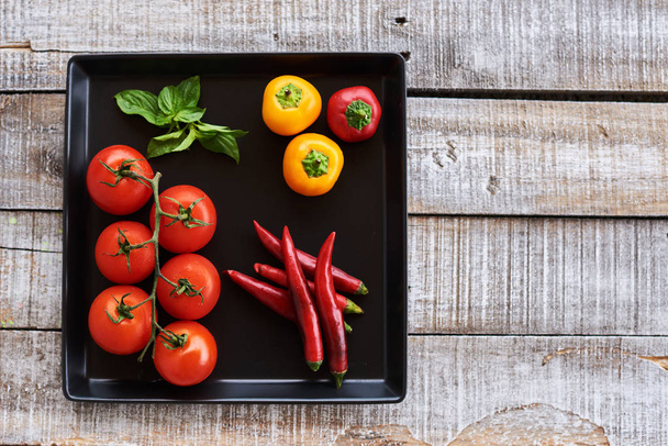 Fresh organic tomatoes, bell pepper, chili, chili on the black  plate  background. Top view. Copy space. - Фото, изображение