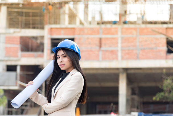 Asian woman architect wearing blue safety helmet checking working progress at construction site. - Fotó, kép