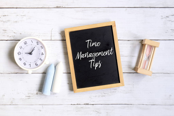 Draufsicht auf Kreide, Tischuhr, Sanduhr und Tafel mit "Zeitmanagement-Tipps" auf weißem Holzgrund. - Foto, Bild