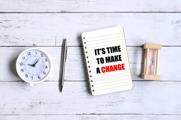 Draufsicht auf Uhr, Sanduhr, Stift und Notizbuch mit inspirierenden Zitaten "es ist Zeit, etwas zu ändern" auf weißem Holzgrund. - Foto, Bild