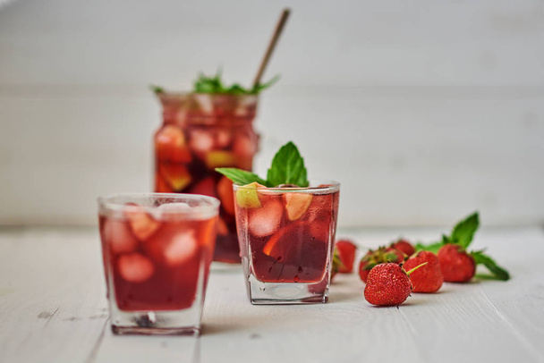Refreshing sangria or punch with fruits in glasses and pitcher.  Traditional summer drink beverage. Red wine, strawberries, oranges, lemon, and green apple. On a wooden rustic table with copy space - Fotografie, Obrázek