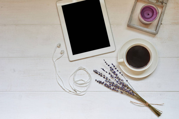 Workspace with cup of black coffee,  digital tablet with empty screen, candle, fresh cookie and flowers on white vintage background. Wireless communication concept. Top view, flat lay, copy space. - Foto, Imagem
