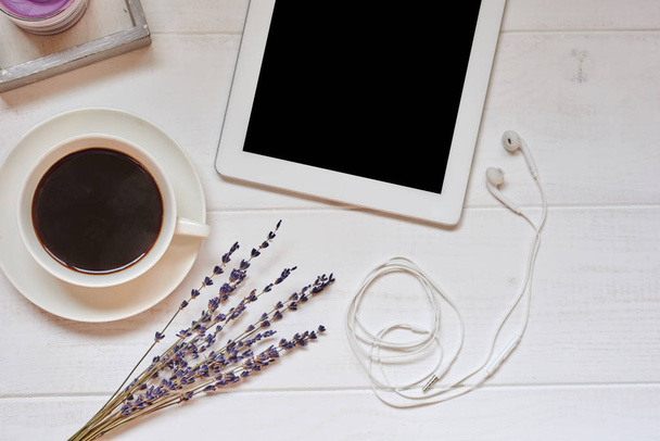 Workspace with cup of black coffee,  digital tablet with empty screen, candle, fresh cookie and flowers on white vintage background. Wireless communication concept. Top view, flat lay, copy space. - Foto, imagen