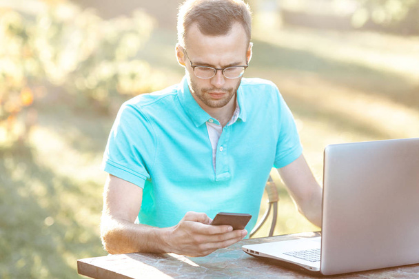 Young business man with glasses uses phone. Freelance work outdoors - Photo, Image