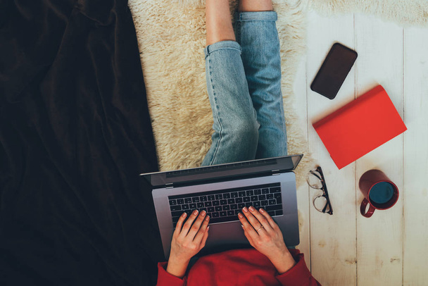 Une jeune femme tenant un ordinateur portable sur ses genoux alors qu'elle était assise à la maison. Femme utilisant un ordinateur portable pour naviguer dans le magasin en ligne. Concept d'achat en ligne. Jeune femme assise sur le tapis à la maison
. - Photo, image