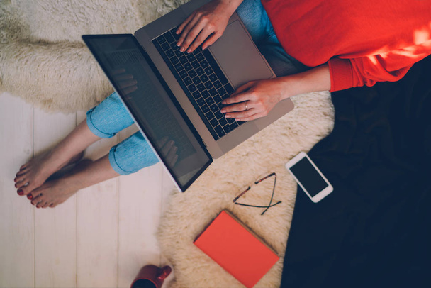 Top view of a young woman holding laptop computer on her lap while sitting at home. Woman using laptop for browsing internet store. Online shopping concept. Young woman sitting on carpet at home - Photo, image