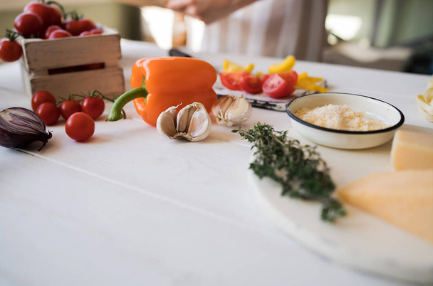 Cheese with fresh vegetables basil and cutting board on white, shabby, rustic kitchen table. Ingredients for cooking on the vintage rural kitchen. Healthy traditional food. Selective focus. Free space - Photo, Image