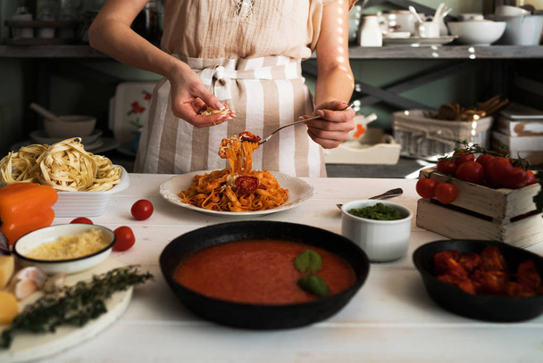Italian style pasta dinner. Pasta with tomato and basil in plate on the wooden rustic table and ingredients for cooking. Chef hands preparing delicious pasta with tomato sous. Homemade food. - Фото, зображення