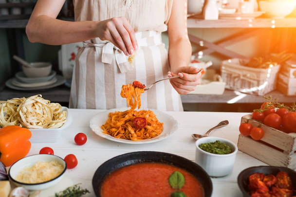 Italian style pasta dinner. Pasta with tomato and basil in plate on the wooden rustic table and ingredients for cooking. Chef hands preparing delicious pasta with tomato sous. Homemade food. - Photo, image