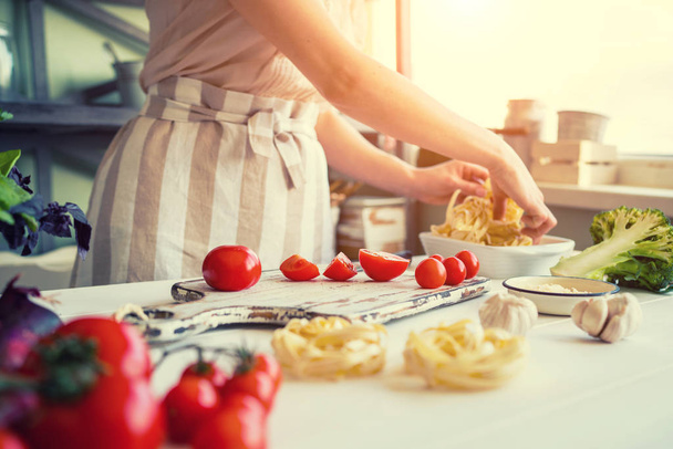 Close up of unrecognizable cook,cutting tomatoes and other vegetables with knife while working in home kitchen. Woman cooking salad, bio food preparing. Vegetarian food, health lifestyle concept. - 写真・画像