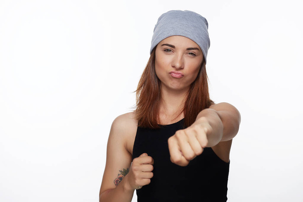 Defend and protection concept. Strong sporty woman wearing casual grey hat, having foxy and confident look, keeping fists clenched in front of her defending herself from jealous girls and bad eye. - Photo, Image