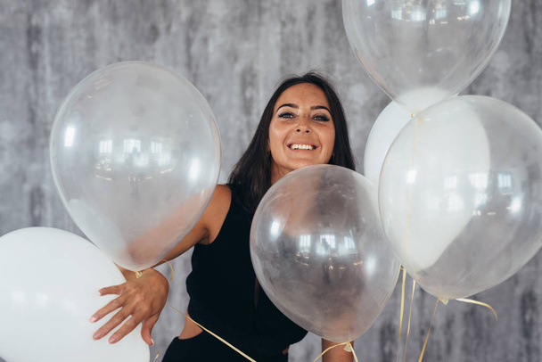 Cute brunette woman standing smiling and playing with balloons. - Foto, imagen