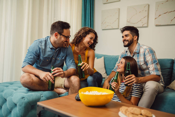 Amigos comiendo palomitas y bebiendo cerveza en casa, divirtiéndose
 - Foto, Imagen