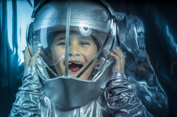 Astronomy, Boy playing to be an astronaut with a space helmet and silver suit on metallic background - Zdjęcie, obraz