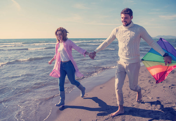 Young couple having fun and playing with kite on beach at autumn day - Foto, Imagen