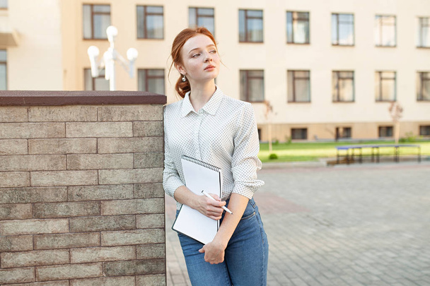 Beautiful red haired girl with freckles hugging notebooks with homework and smiling happy. Back to school concept. Portrait of a student - Valokuva, kuva