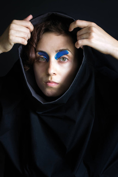 imagem de moda foto close-up menina com cabelo encaracolado em roupas pretas com tinta azul na frente de seus olhos para fora do capô
 - Foto, Imagem