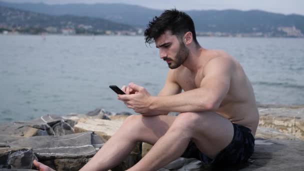 Άνθρωπος στη θάλασσα χρησιμοποιώντας κινητό τηλέφωνο για να πληκτρολογήσετε το μήνυμα - Πλάνα, βίντεο
