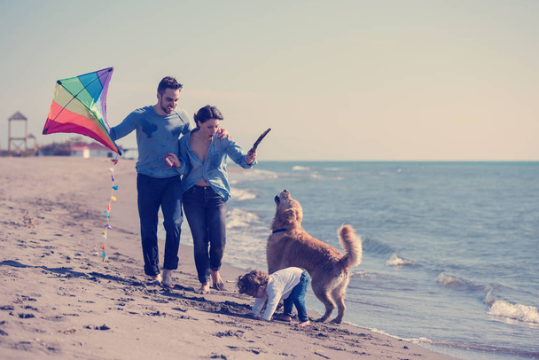счастливая молодая семья с детьми, развлекающимися с собакой и змеей на пляже в осенний день - Фото, изображение
