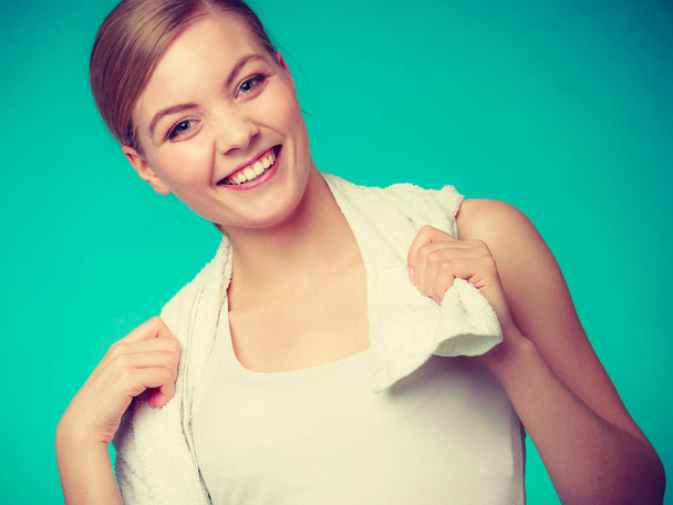 Workout, hygiene concept. Smiling woman holding a towel around her shoulders smiling at the camera, studio shot on blue background - 写真・画像
