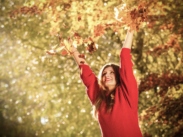 ευτυχία ξέγνοιαστες. χαλαρωτικό γυναίκα σε φθινόπωρο πάρκο που ρίχνουν τα φύλλα επάνω στον αέρα με τα χέρια προς τα πάνω. όμορφο κορίτσι στο πολύχρωμο δασών φύλλωμα εξωτερική. - Φωτογραφία, εικόνα